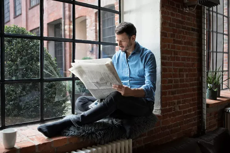 Man sat on window ledge reading newspaper